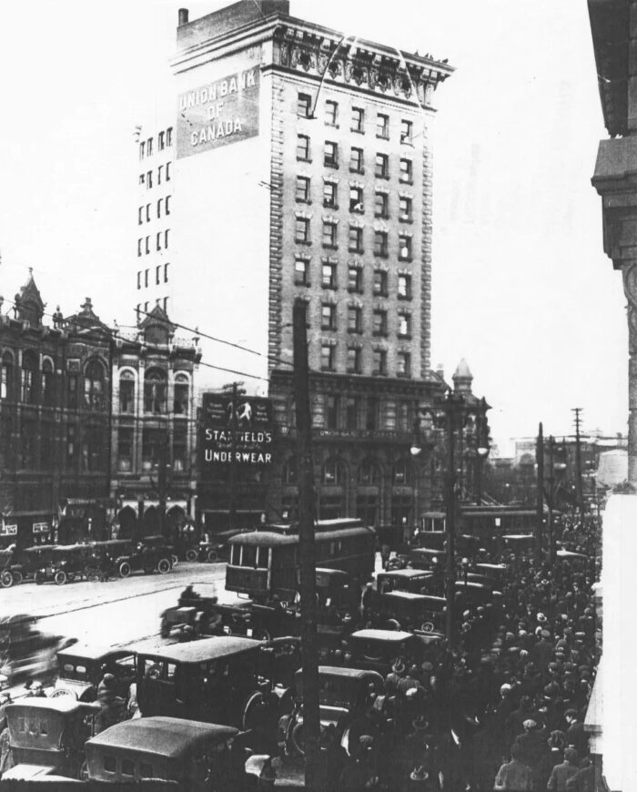 The Union Bank Tower with antique vehicles, streetcars, people and street lights on the street and sidewalk in front.