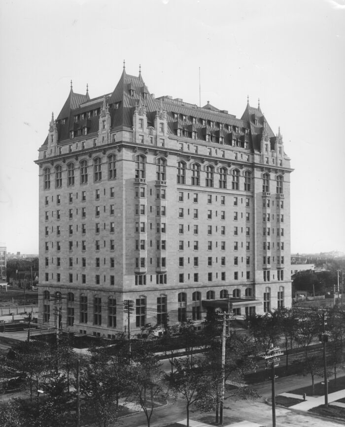 The Fort Garry Hotel with trees, streets and power lines on wooden poles in front.