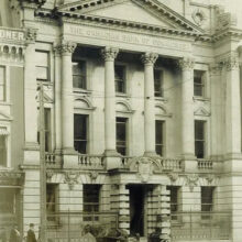 Image 2: Winnipeg’s Bank of Commerce (Millennium Centre) with people and antique vehicles on the sidewalk and street in front.