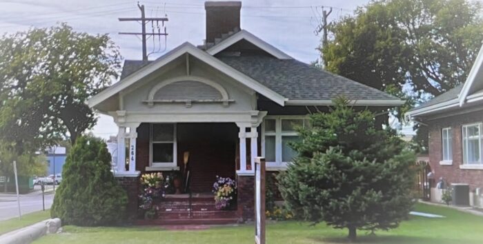 The Peters Bungalow with flowers and a broom on the front steps. A tree obscures part of the facade.