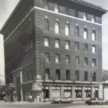 Image 1: Archival black and white photo of the Travellers Building looking west down Bannatyne Avenue from the corner of William and Bannatyne