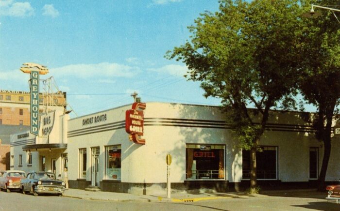 Single-storey with neon signs indicating bus depot and grill, with facade rounded to right side of building with restaurant windows.