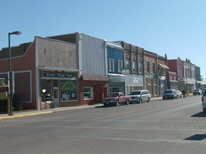 Main Street in Carberry with various businesses. Multiple vehicles are parked along the sidewalk.