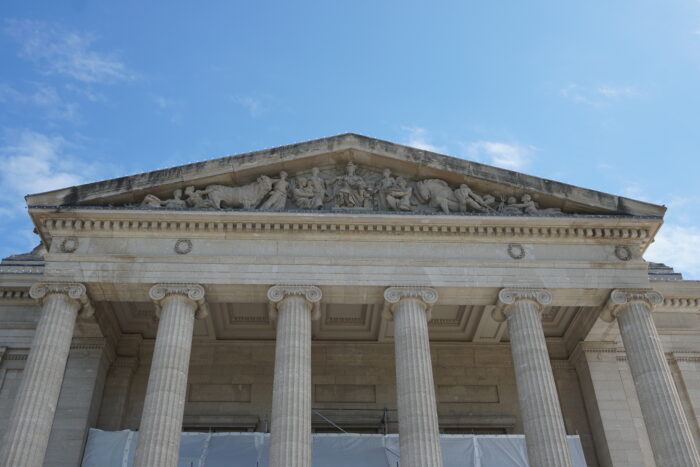 A pediment with stone statues of people and animals rest on six large Ionic-style columns.