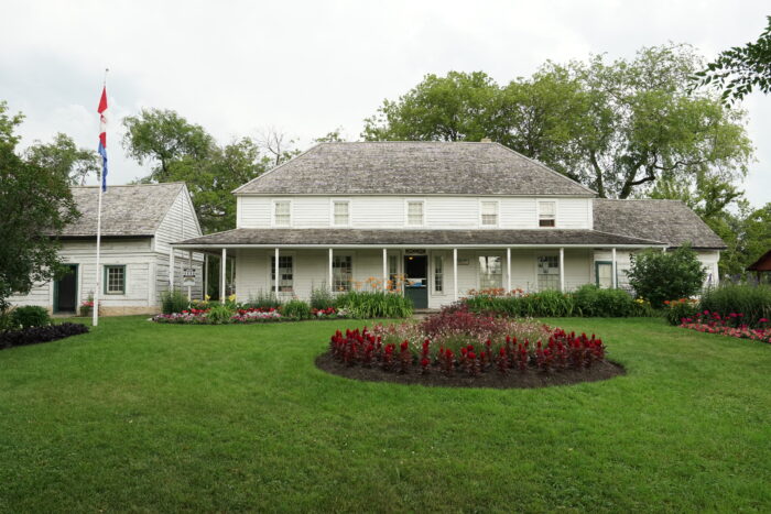 Seven Oaks House Museum with flowerbeds and a flagpole in front.