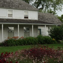 Image 4: A partial facade of the Seven Oaks House featuring the white slatted exterior and front landscaping