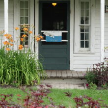 Image 6: The green wooden front door of the Seven Oaks House under a covered porch