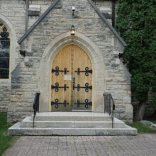 Image 1: Steps up to a large wooden doors with iron detailings that lead into the cathedral