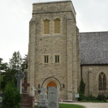 Image 8: Facade of St. John's Cathedral with grave markings in view on the grass towards the left and a path towards the right leading up to the doors