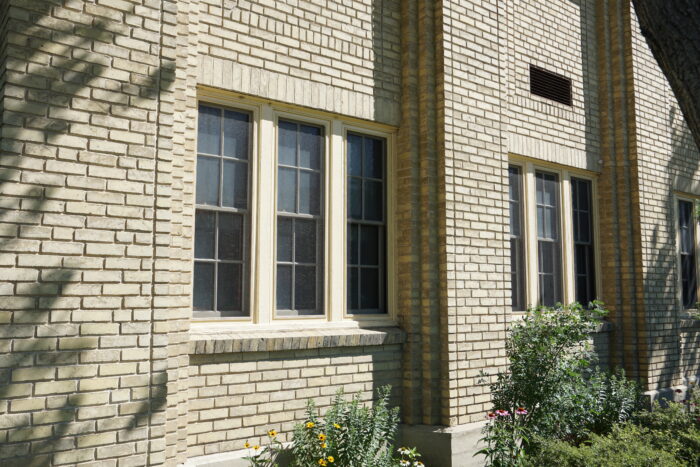 Windows on the facade of the Women’s Tribute Memorial Lodge with plants growing in front.