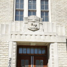 Image 4: Ornamental details featuring a crest above the front door on the front facade of the building