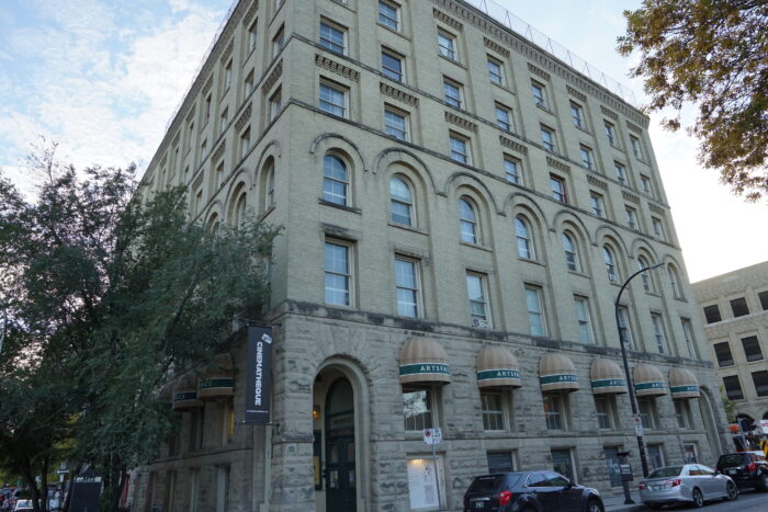 The Gault Building (Artspace) with a sign reading “CINEMATHEQUE” at the entrance. Vehicles are parked along the sidewalk.