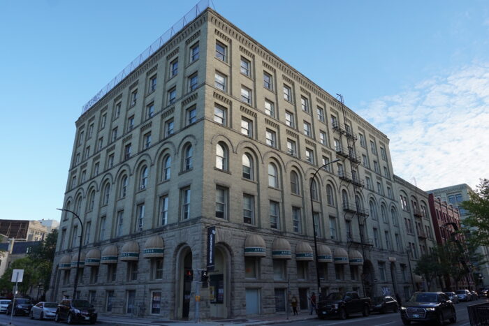 The Gault Building (Artspace) with vehicles parked along both sides. Two people walk on the sidewalk.