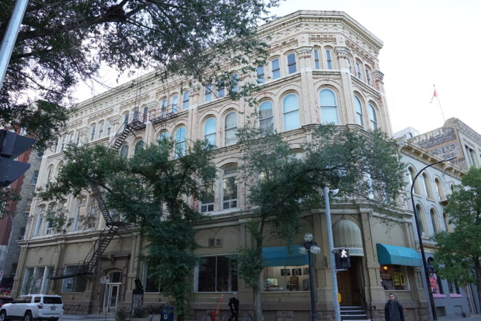 The Telegram Building with two sidewalk trees partially obscuring the facade. Two people walk by.