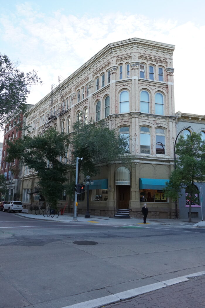 The Telegram Building with sidewalk trees partially obscuring the facade. A person stands in front.