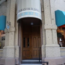 Image 3: Entrance of the Telegram Building at the corner of Albert and McDermot from street level featuring covered steps to the front door with text above that reads "Telegram Building, 70 Albert Street"