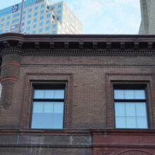 Image 1: Looking up the facade of the building featuring 2 glass paned windows and details of the cornice