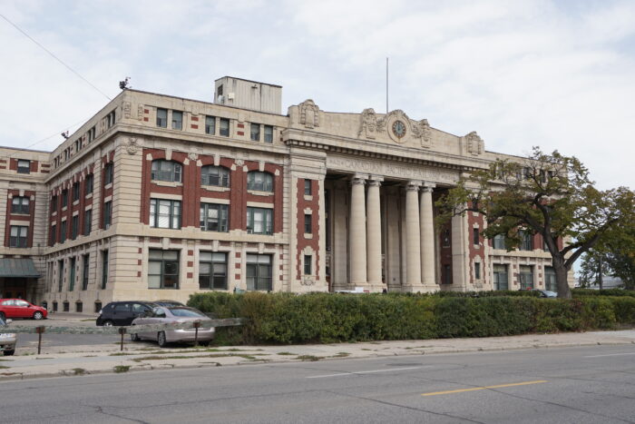 Winnipeg’s Canadian Pacific Railway Station building behind a hedge. Vehicles are parked in the lot beside the building.