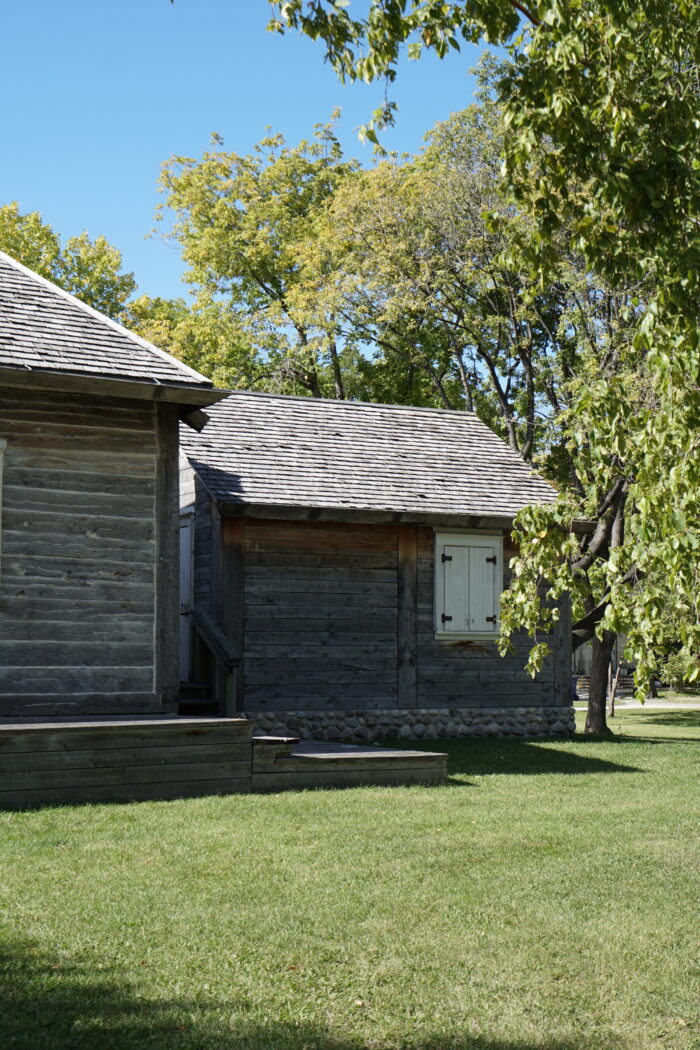 The small out building next to Ross House with the shutters closed. Trees grow in the background.