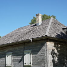 Image 2: An older wooden house featuring white wooden window covers and a small chimney on the roof