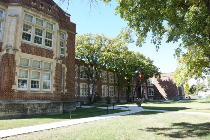 Daniel McIntyre School with trees and a flag pole flying the Canadian flag in front.