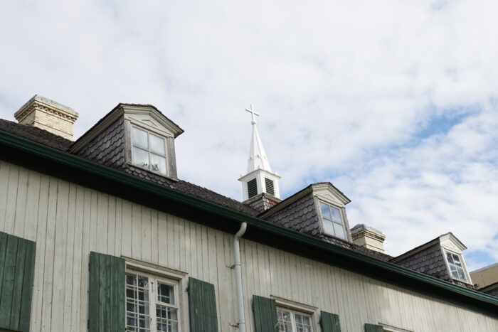 The roofline of the St. Boniface Museum. Dormers and a spire topped with a cross project upwards.