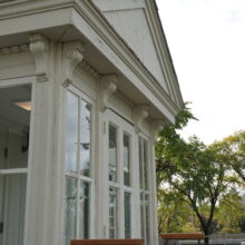 Image 8: Enclosed entrance into St. Boniface Museum featuring a pediment above the door and a raised porch with red railing