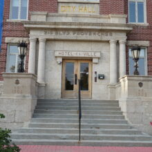 Image 3: Stairs leading up to the front doors of the St. Boniface City Hall with markings above the door that reads "Hotel de Ville", "219 BLVD Provencher, "City Hall"