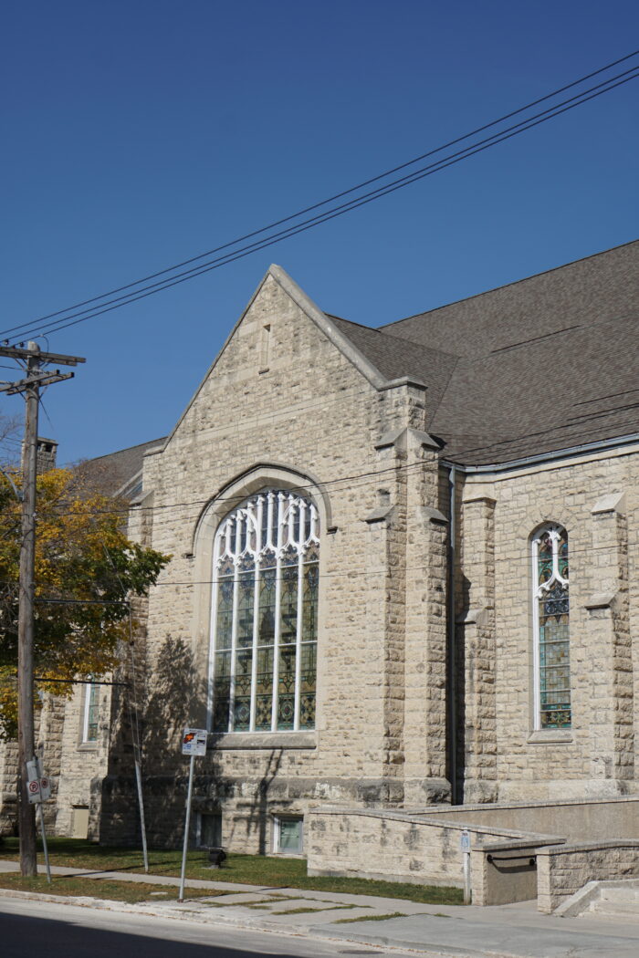 A side facade of Winnipeg’s Westminster Church with a bus stop and power lines in front.