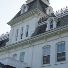 Image 4: View of the top half of the building's facade featuring dormer windows on the grey roof and black iron parapets closer to the top