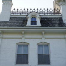 Image 5: Two second floor windows against the white wall and a dormer window on the grey roof featuring a small chimney to the left