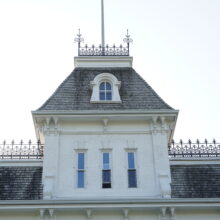 Image 6: A small portion of the third floor of the house featuring 2 narrow rectangular windows, a dormer window, parapets and a flag pole