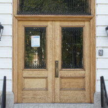 Image 8: Small steps with black railings leading to a set of large wooden doors with two glass panes and small window above at the front of Government House