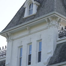 Image 10: A small portion of the third floor of the house featuring 2 narrow rectangular windows, a dormer window and parapets viewed from an angle