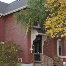 Image 1: Kelly House with trees and bushes growing around it, obscuring the facades.