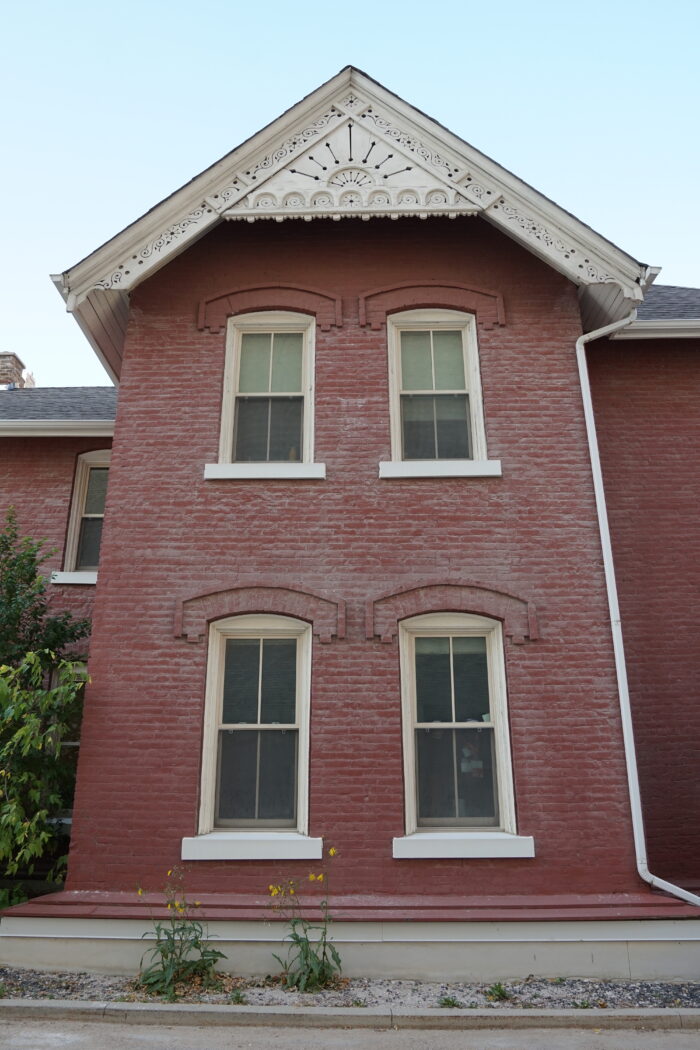 Windows on the side of Kelly House with ornate trim under the roofline. Weeds grow in front of the facade.