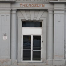 Image 4: Osborne Street entrance of the Roslyn Court Apartments with decorative details on the arch and a sign that reads "The Roslyn" in red against the grey