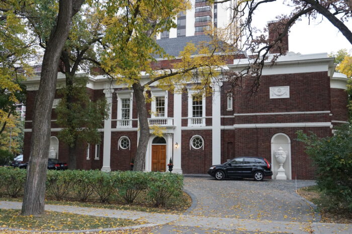 Moss House with two vehicles parked in the driveway. Trees in the yard obscure part of the facade.