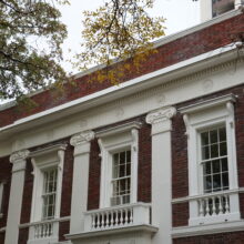 Image 2: Second floor windows of Moss House featuring white Juliette balconies and white pilasters against the red brick facade