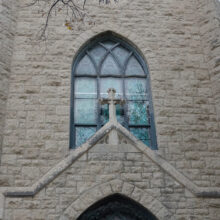 Image 10: Coloured glass paned large window above the entrance of the church featuring intricate detailing