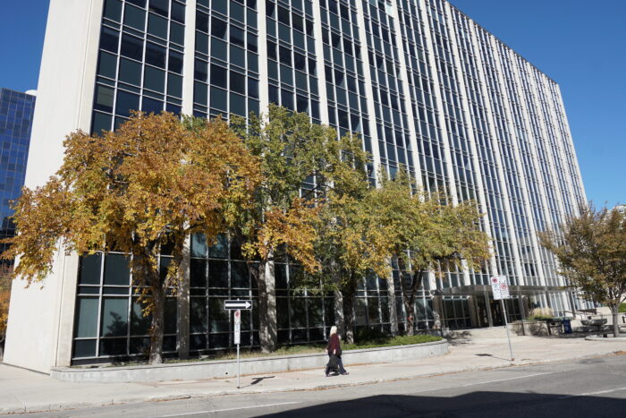 The Norquay Building with trees growing in front. A person walks by on the sidewalk.