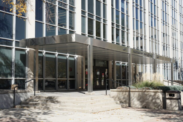 The front entrance of the Norquay Building with a planter and garbage can in front.