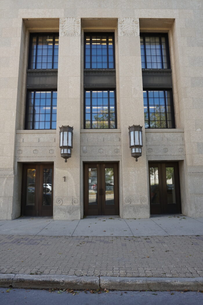 An entrance to Winnipeg’s Civic Auditorium building. Two large light fixtures sit between three sets of double doors.