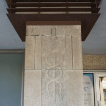 Image 2: Close up of a column near the entrance of the building featuring a caduceus symbol