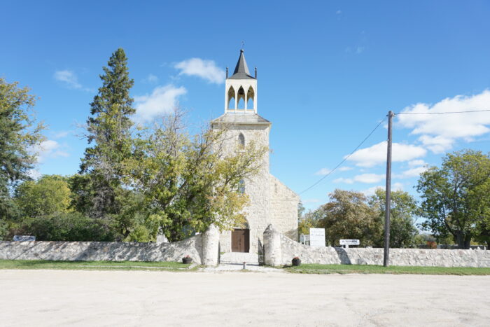 St. Andrews Church behind a stone wall with an open gate. A tree obscures part of the facade.