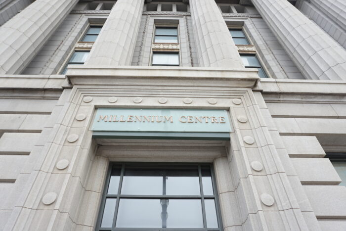 Looking up at the front facade of Winnipeg’s Bank of Commerce (Millennium Centre) with a sign that reads “MILLENNIUM CENTRE.”