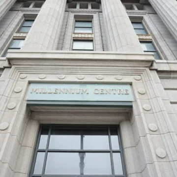 Looking up at the front facade of Winnipeg’s Bank of Commerce (Millennium Centre) with a sign that reads “MILLENNIUM CENTRE.”