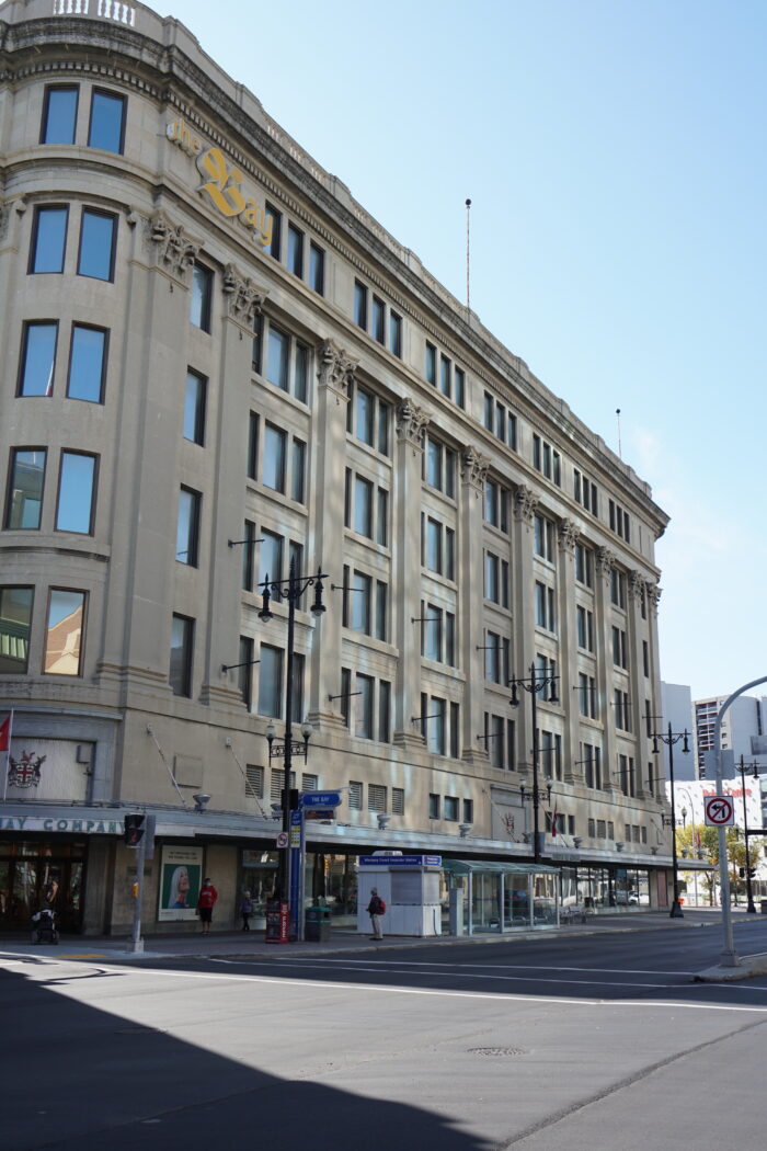 Winnipeg’s Hudson’s Bay Company Downtown Store with people, a bus shelter and street lights in front.