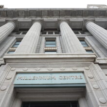 Image 6: Looking up at the facade of the Canadian Bank of Commerce featuring columns and architectural details with Millennium Centre sign visible