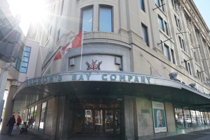 Above the wooden-framed glass door, a canopy with metal letters reads 'Hudson's Bay Company.' Above the canopy are the Hudson's Bay Company's coat of arms and a Canadian flag.